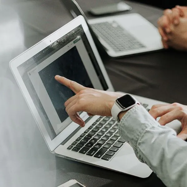 Two people at a table, one pointing at a laptop screen